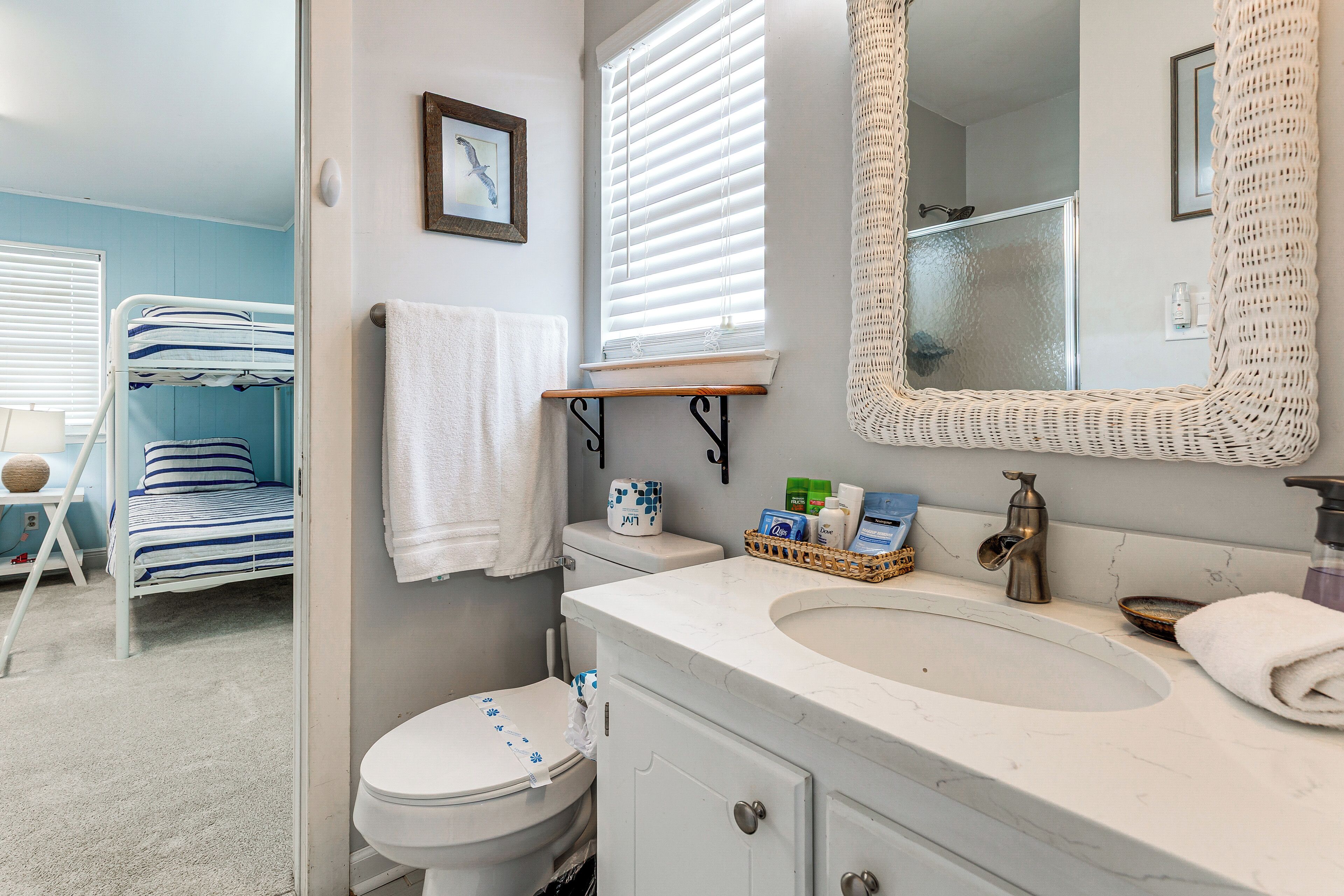 A bathroom with a white sink, a mirror, a toilet, and a bunk bed in the adjacent room.