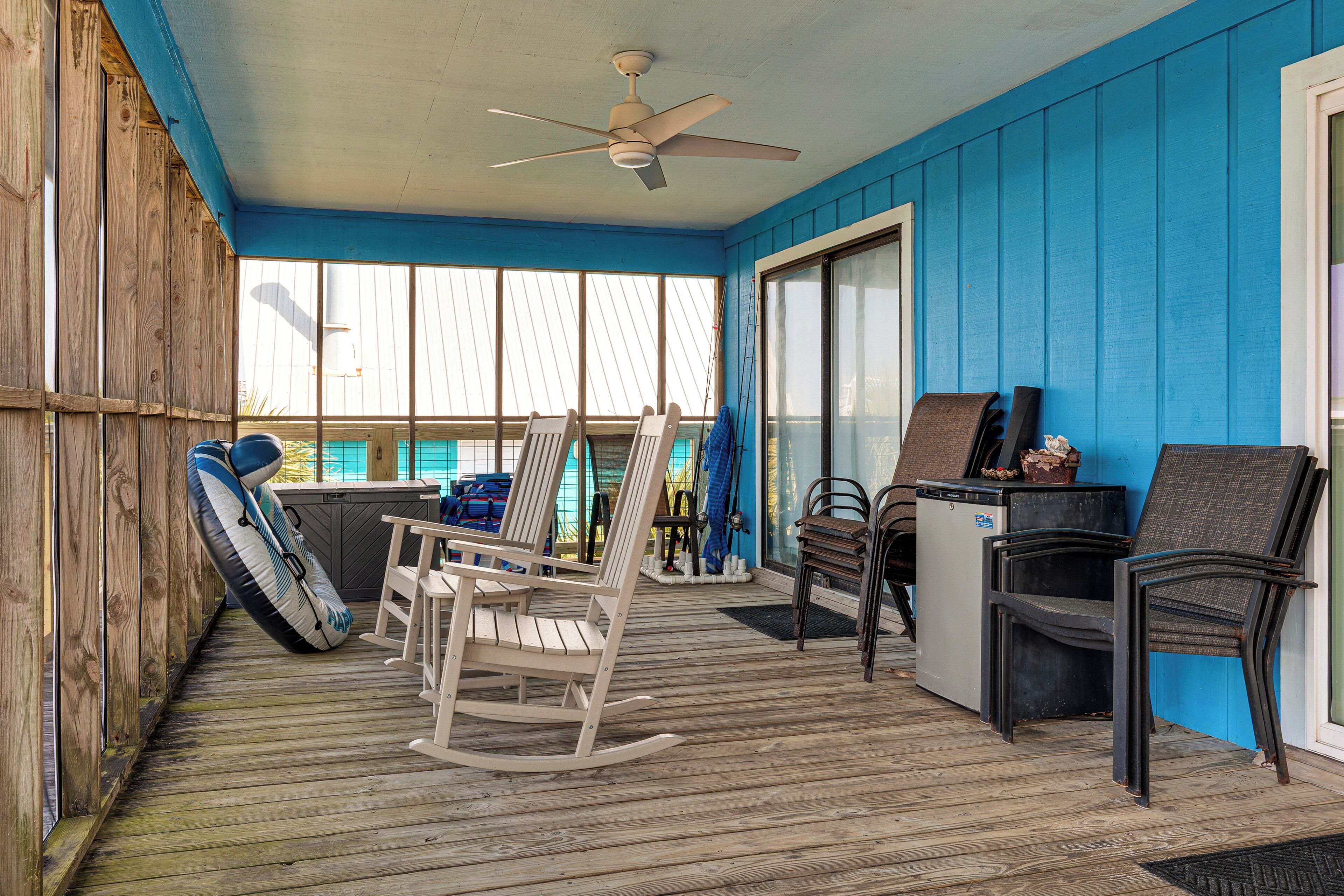 Une terrasse couverte avec un plancher en bois, un ventilateur de plafond et divers types de sièges, notamment des chaises et un fauteuil à bascule.