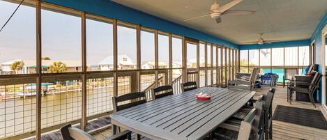 A covered outdoor dining area with a table and chairs, large windows, and a ceiling fan.