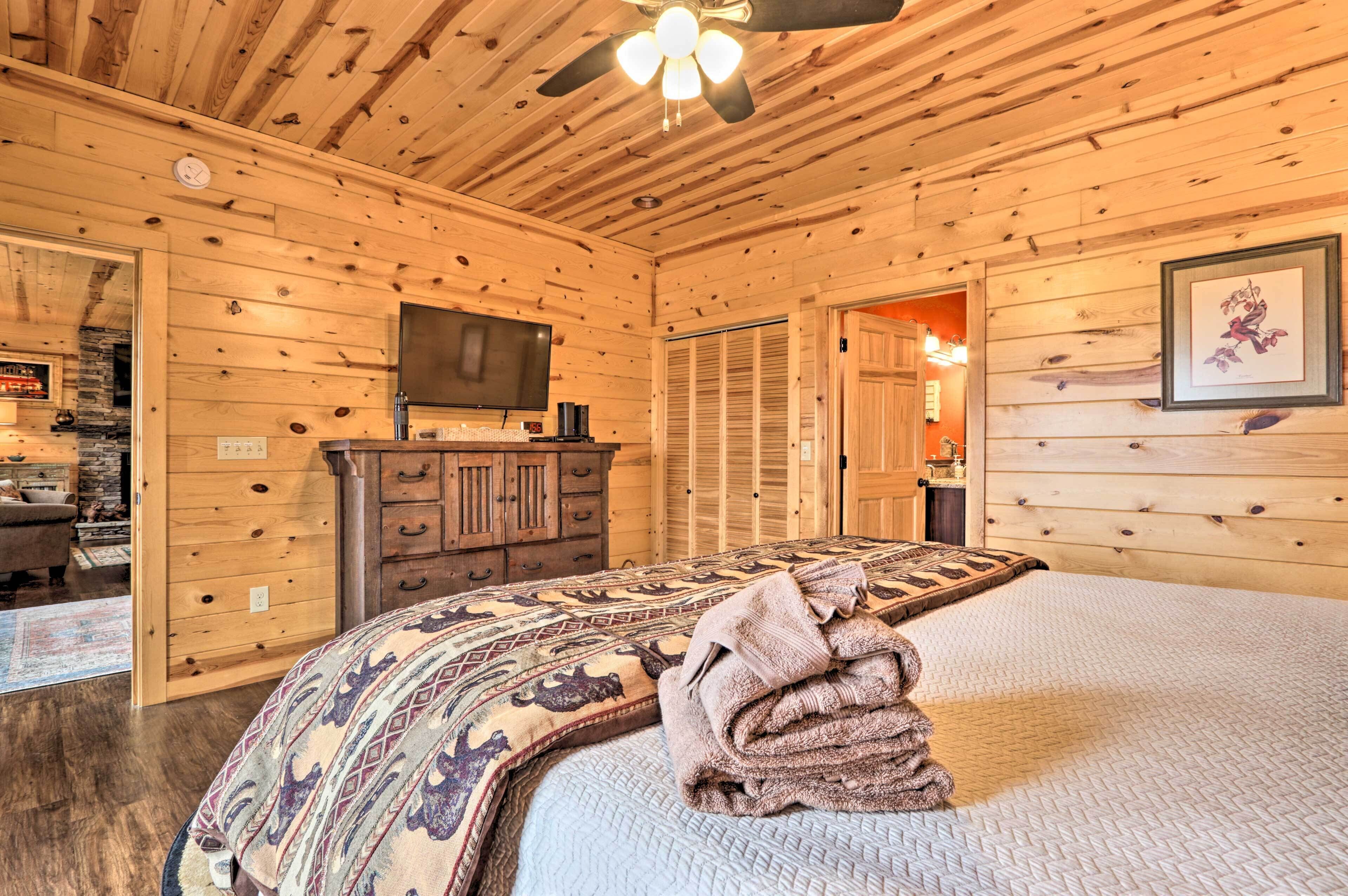 A wooden-paneled room with a bed, a television, a dresser, and a door leading to another room.