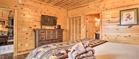 A wooden-paneled room with a bed, a television, a dresser, and a door leading to another room.