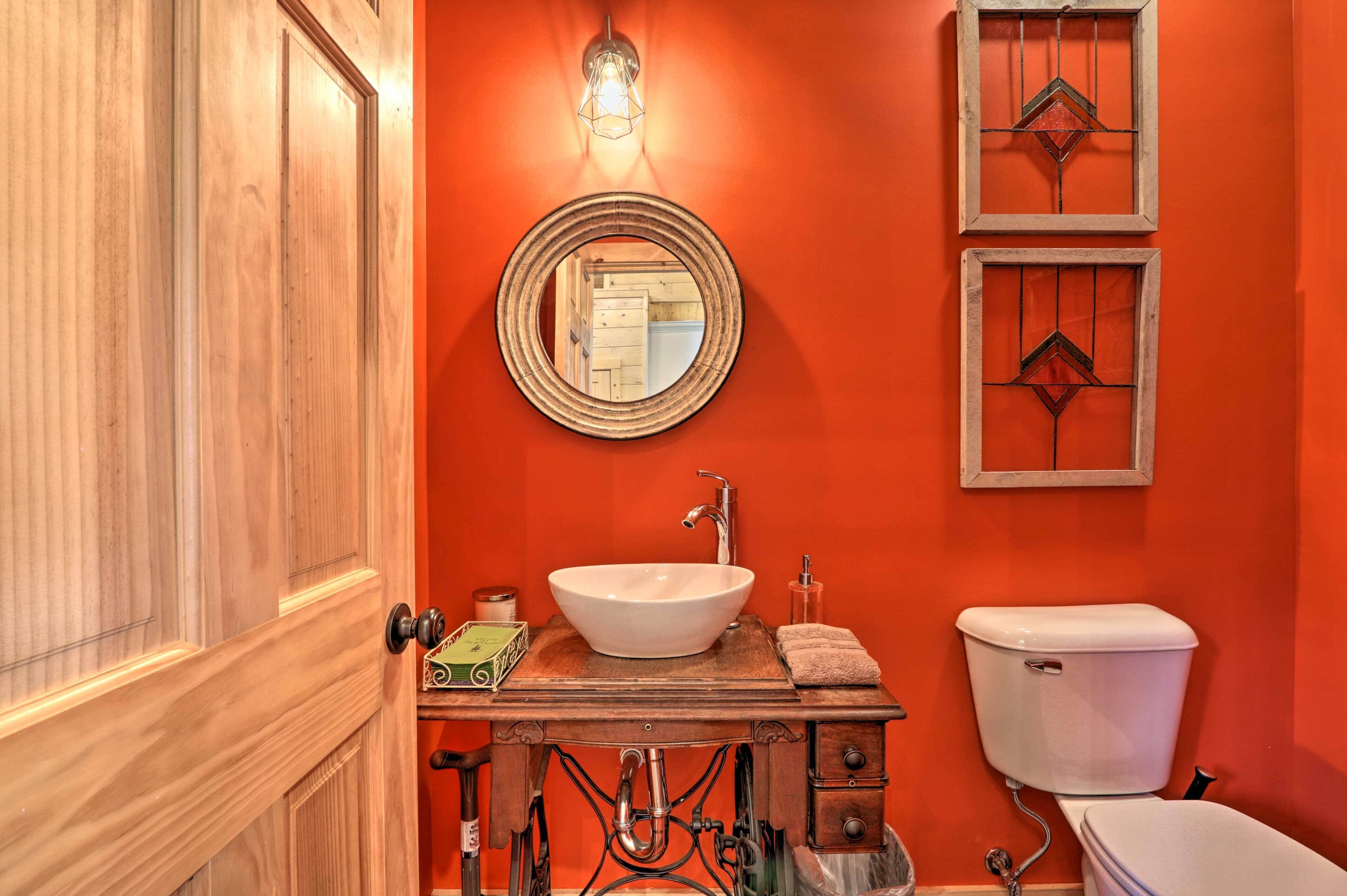 A bathroom with a wooden vanity, a white sink, and a toilet. There are two wall-mounted mirrors and a light fixture above the vanity.