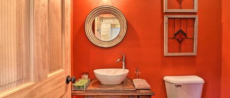 A bathroom with a wooden vanity, a white sink, and a toilet. There are two wall-mounted mirrors and a light fixture above the vanity.