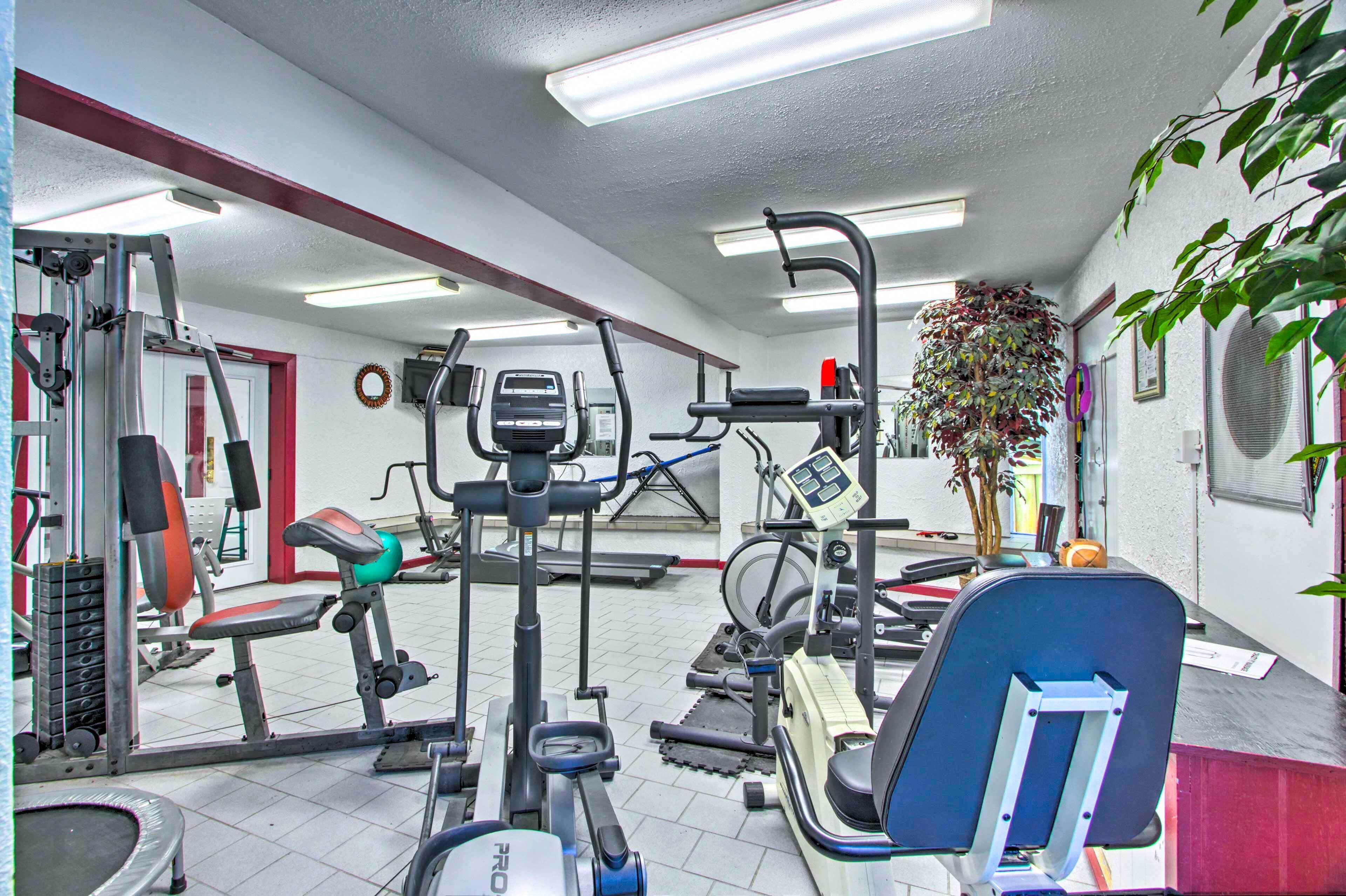 Un gimnasio con equipo de ejercicio variado, una cinta de correr y una televisión montada en la pared.