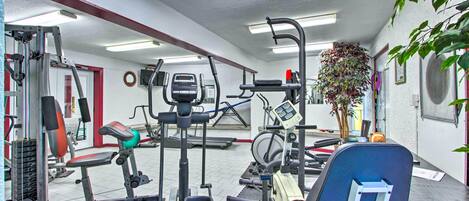 Un gimnasio con equipo de ejercicio variado, una cinta de correr y una televisión montada en la pared.