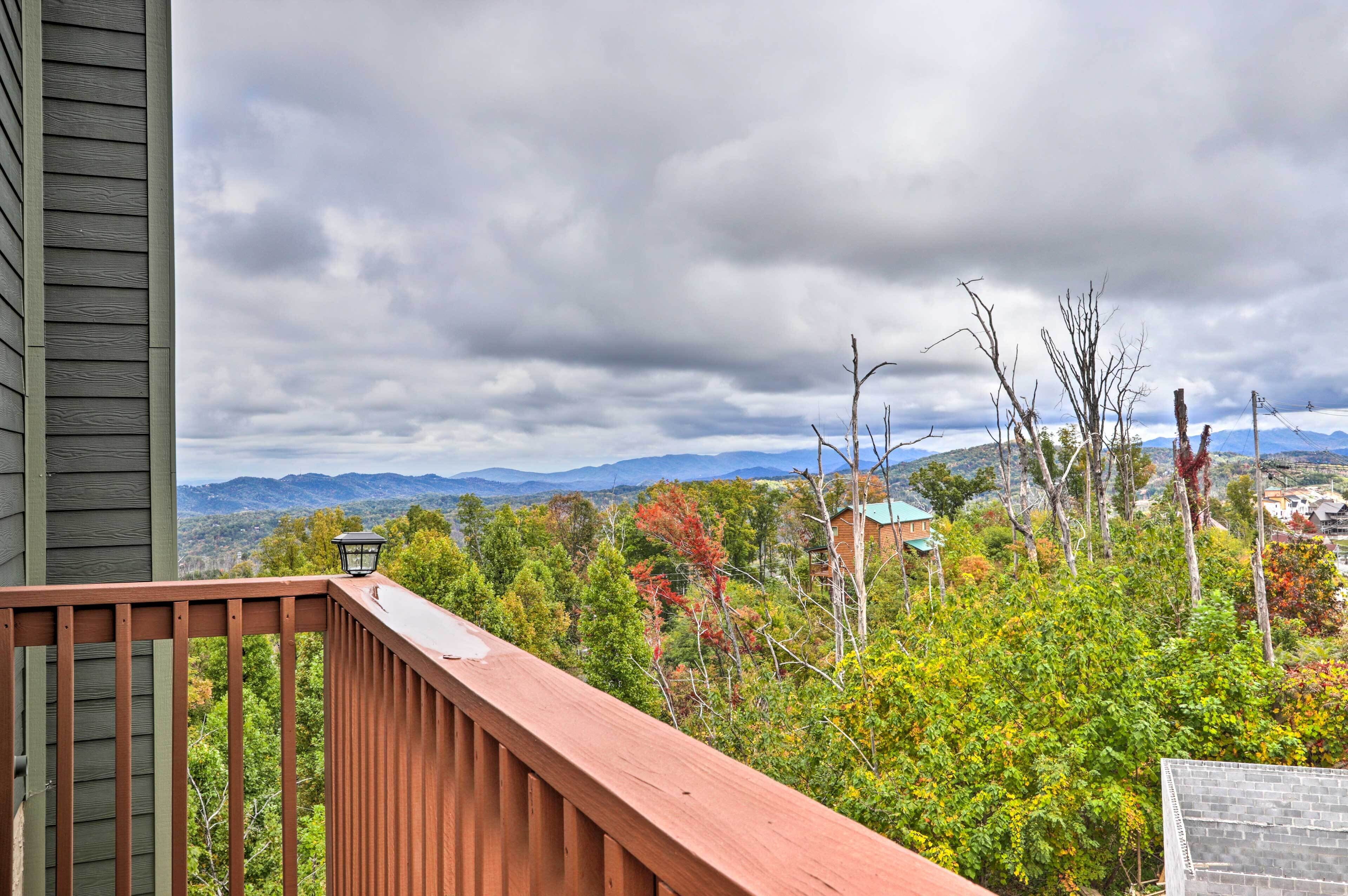 Une terrasse en bois, ornée d’une lanterne, qui offre une vue sur un paysage montagneux aux couleurs automnales, sous un ciel nuageux.