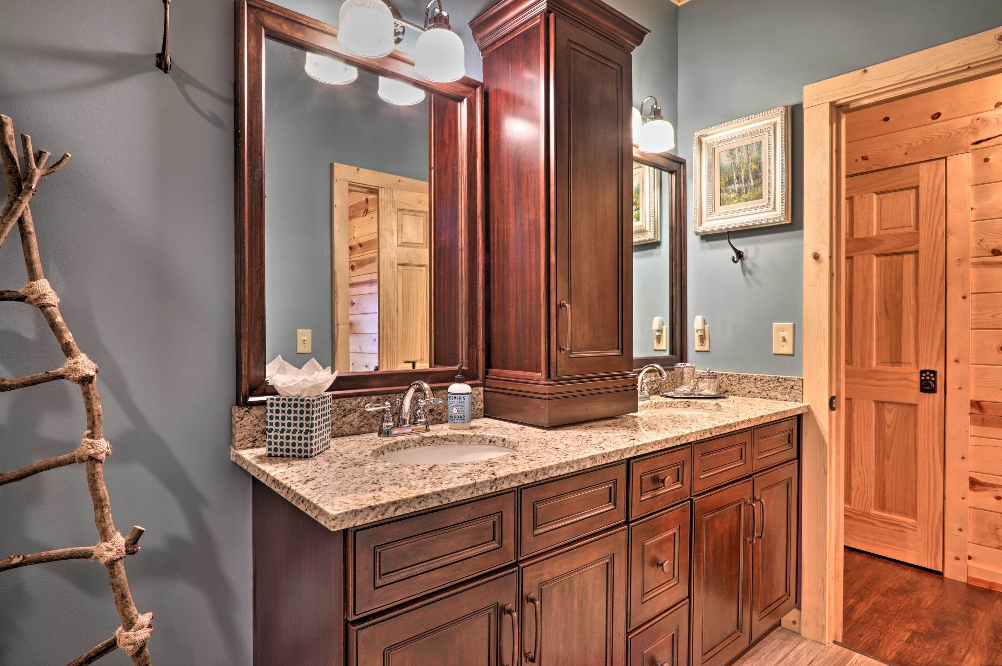 A bathroom with a double sink vanity, wooden cabinets, a large mirror, and a wooden door.