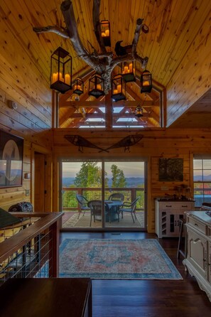 A wooden cabin interior with a large tree branch chandelier, a dining area with chairs, and a view through the glass doors. - Woodsy Retreat w/ Fire Pit & Resort Amenities (Gatlinburg)