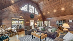 Una sala de estar espaciosa con paredes de madera, un comedor con mesa y sillas, y una zona de estar acogedora con sofá y sillones.