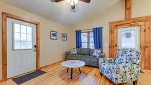 A living room with a wooden floor, a ceiling fan, a gray sofa, a patterned armchair, and a coffee table. - Waynesville Cabin Rental w/ Mountain Views (Waynesville)