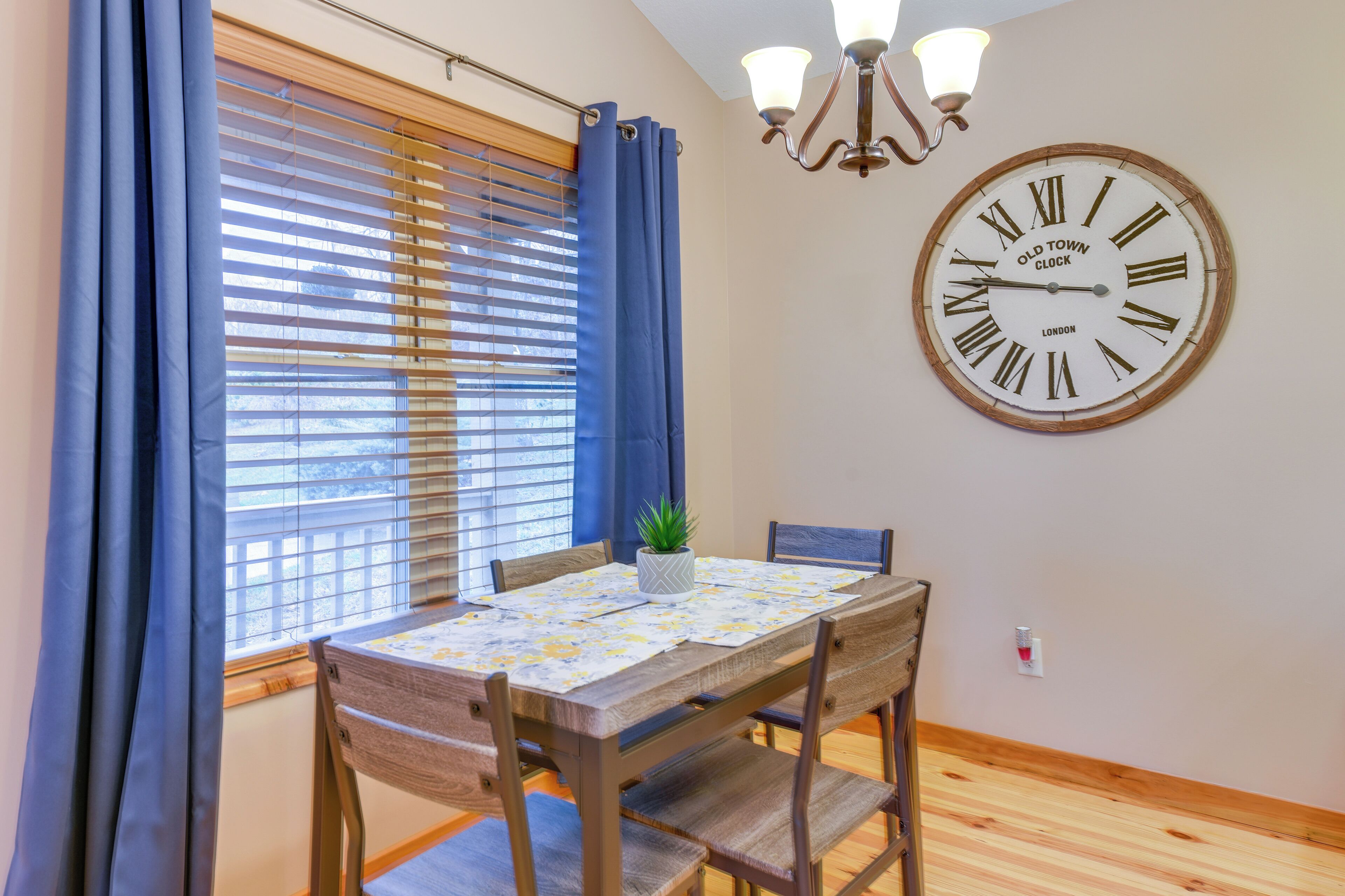 A dining area with a wooden table, chairs, a potted plant, and a large wall clock.