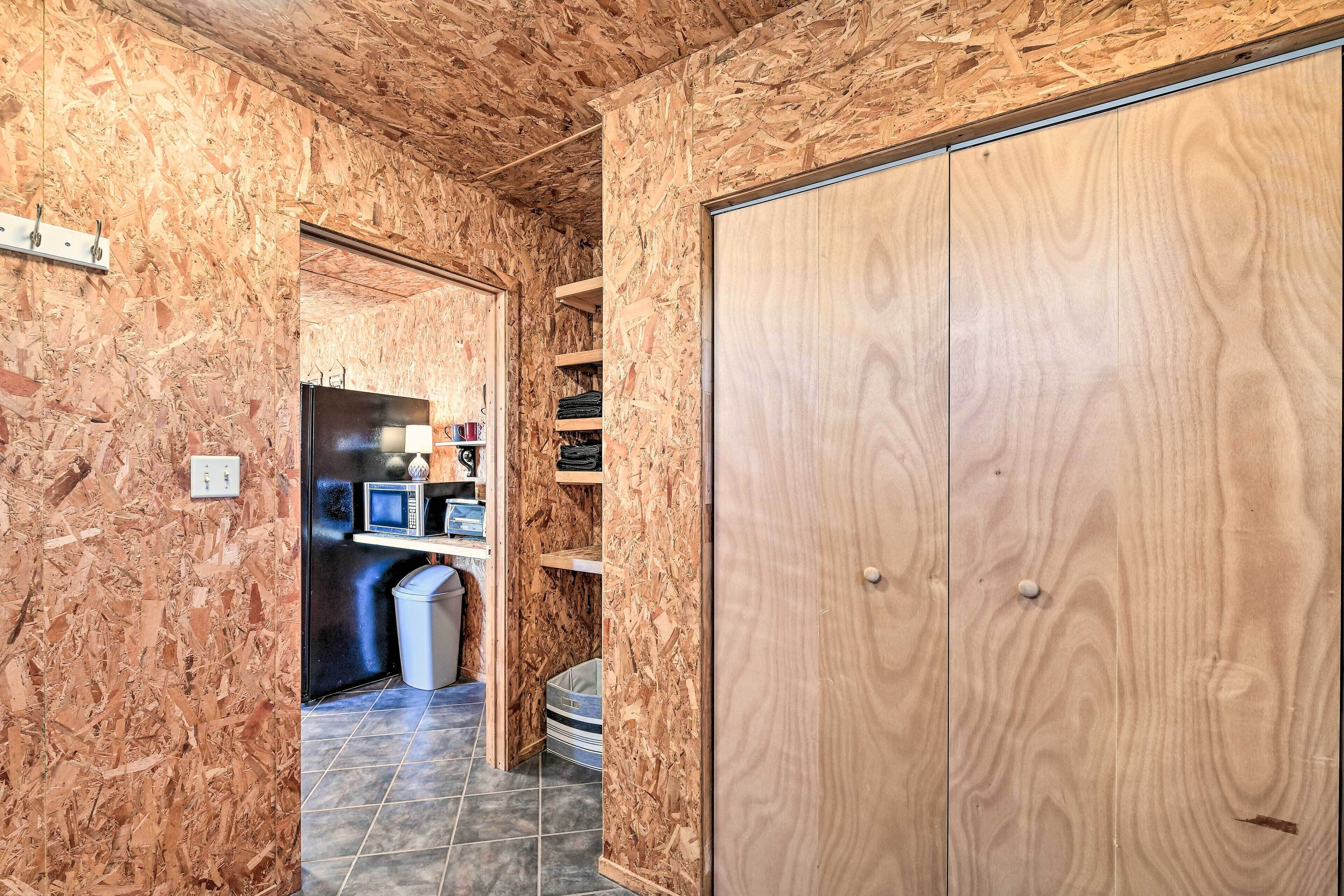 A room with wooden walls and a large wardrobe. There is a small desk with a computer and shelves with various items.