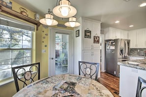 A kitchen with white cabinets, a stainless steel refrigerator, and a dining area with a table covered in a floral tablecloth.