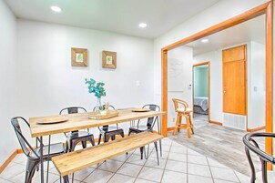 Uma área de refeições com mesa de madeira, cadeiras e um banco. Há duas imagens emolduradas na parede.