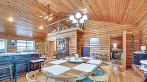 A wooden cabin interior with a dining table, chairs, a kitchen area, and a loft bedroom. - Kentucky Group Getaway w/ Dock + Lake Access (Burnside)