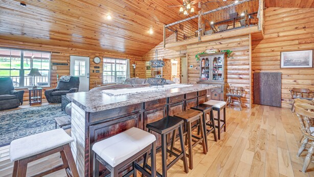 A spacious log cabin with a large kitchen island, multiple bar stools, and a cozy seating area with a fireplace. - Kentucky Group Getaway w/ Dock + Lake Access (Burnside)