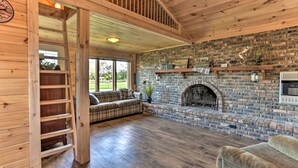 A cozy living room with a fireplace, wooden floors, a plaid sofa, and a wooden ladder. - Waterfront Syracuse Home: Deck, Fire Pit & Kayaks (Syracuse)