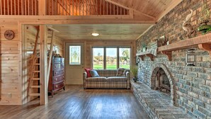 A cozy room with a wooden floor, a plaid sofa, a fireplace, and a brick wall. - Waterfront Syracuse Home: Deck, Fire Pit & Kayaks (Syracuse)
