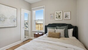 A bedroom with a bed, a nightstand, a window, and wall art. - Chic, Luxurious Sunnyside Home (Denver)