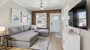 A modern living room with a sectional sofa, a flat-screen TV, and a brick accent wall. - Chic, Luxurious Sunnyside Home (Denver)