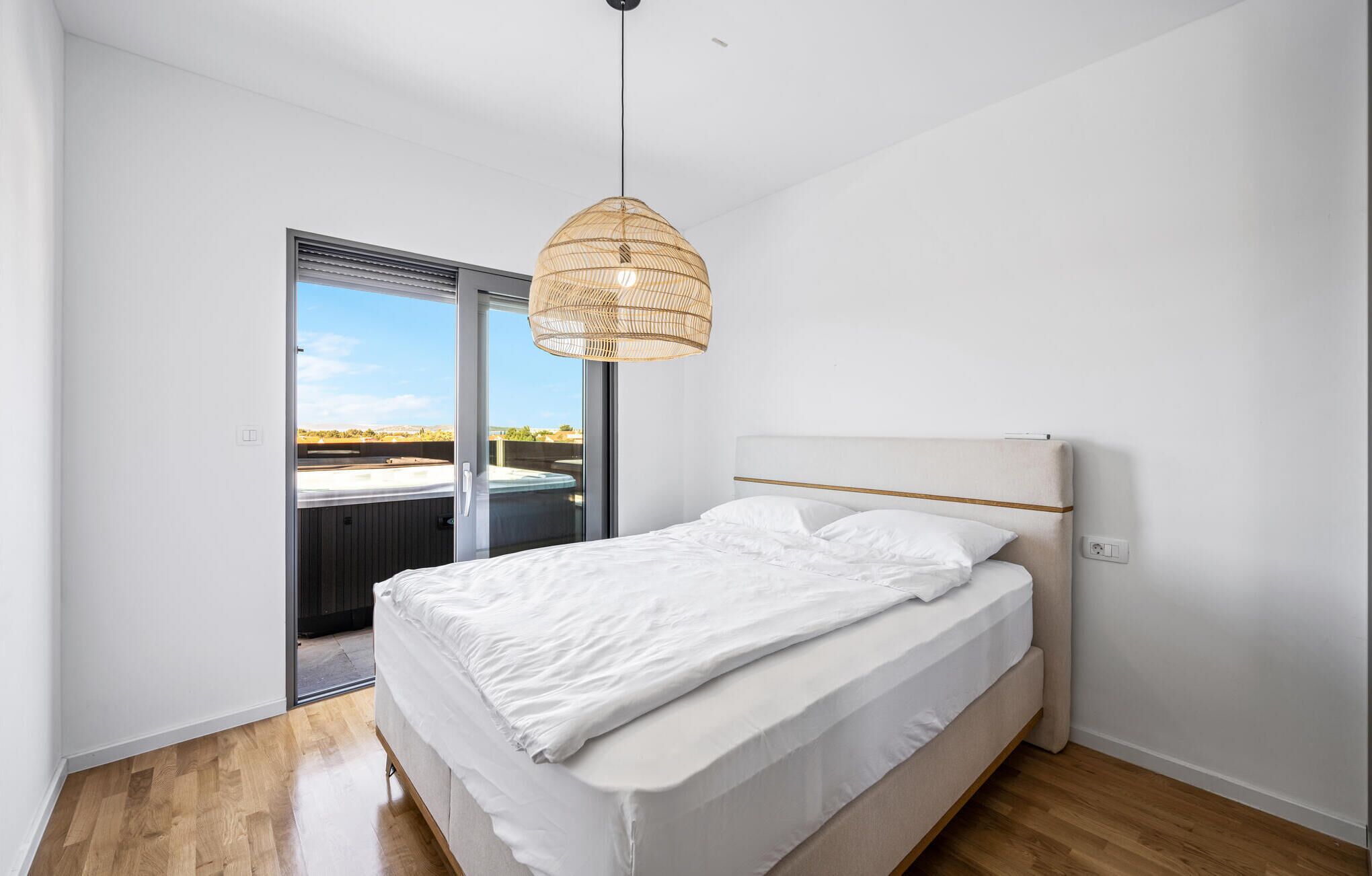 Une chambre avec un lit, un luminaire suspendu, une porte-fenêtre coulissante donnant sur un balcon et une vue sur un jacuzzi.