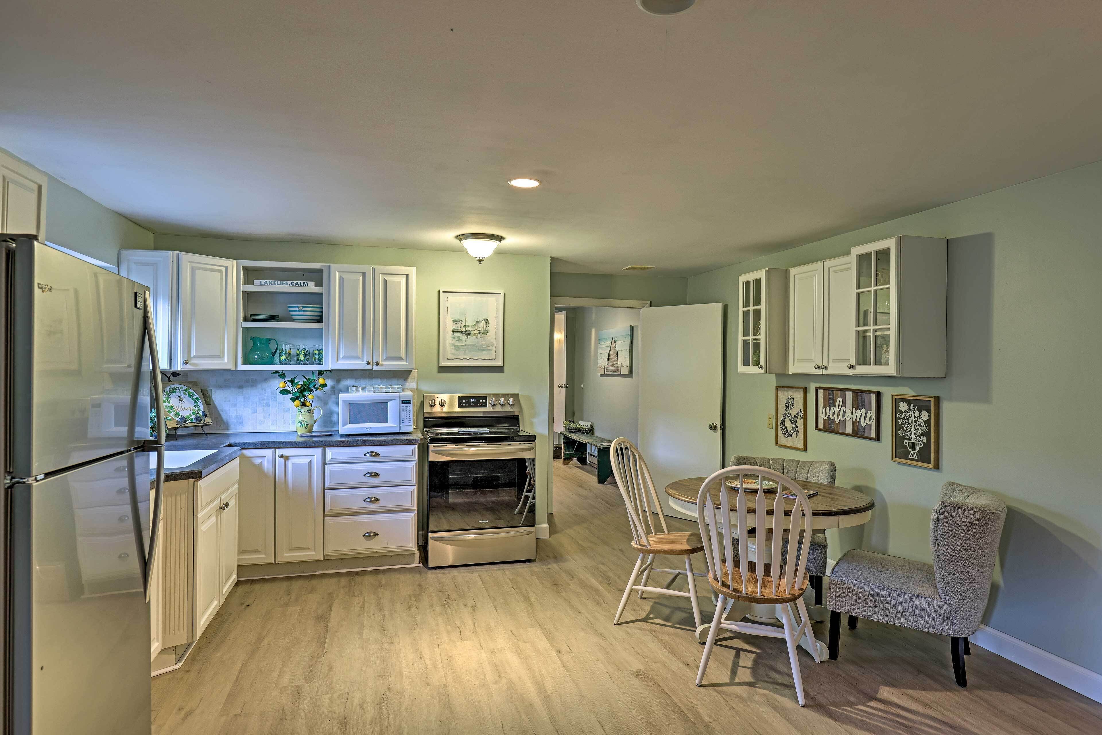 A kitchen with white cabinets, a refrigerator, an oven, a microwave, and a dining area with a table and chairs.