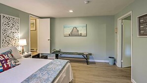 A bedroom with a bed, a bench, a painting, and a door.