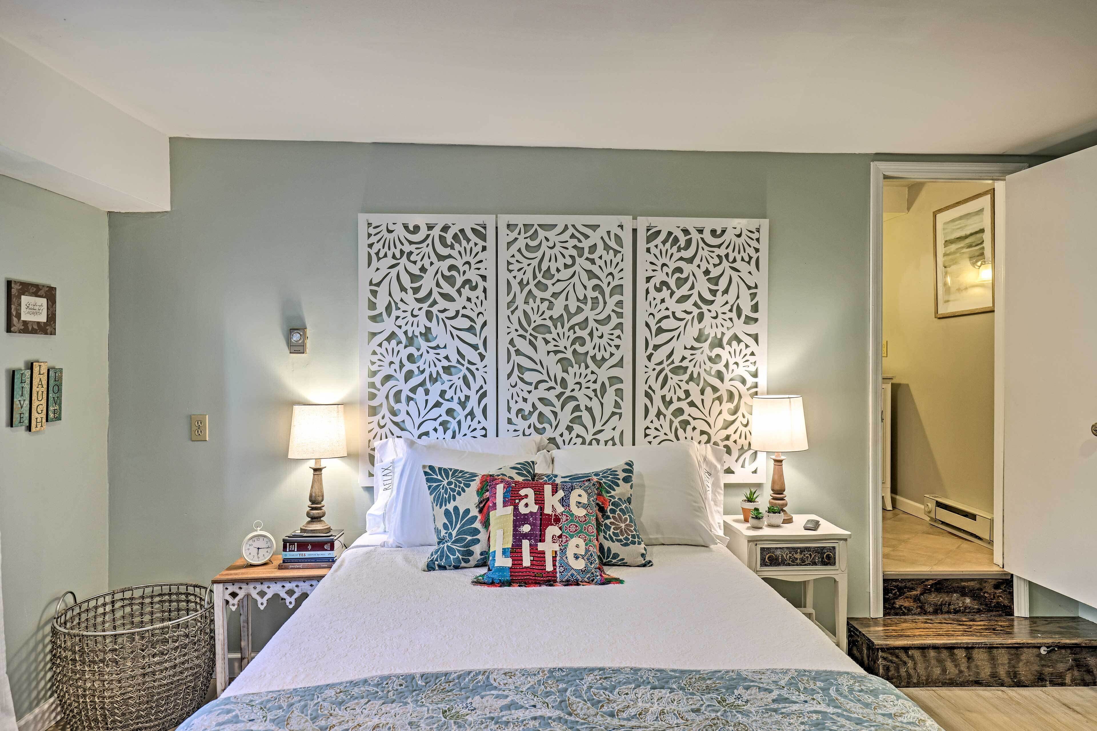 Une chambre à coucher bien rangée, avec un lit, deux tables de chevet dotées de lampes, une tête de lit décorative et une petite table de chevet sur laquelle se trouvent des livres et une horloge.
