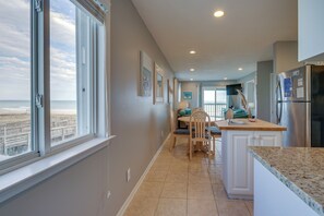A kitchen with a view of the beach, a dining area with chairs and a table, and a refrigerator. - Steps to Boardwalk: Carolina Beach Condo w/ Views! (Carolina Beach)