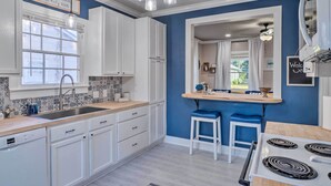 A modern kitchen with white cabinets, a large window, and a blue accent wall. - Central Cottage w/ Grill, 1 Mi to Cajun Field (Lafayette)