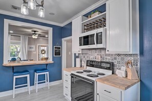 A kitchen with a blue wall, white cabinets, a stove, and two bar stools. - Central Cottage w/ Grill, 1 Mi to Cajun Field (Lafayette)