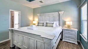 Ein Schlafzimmer mit einem großen Bett, zwei Nachttischen, einem Beistelltisch und einer Tür zu einem anderen Raum.