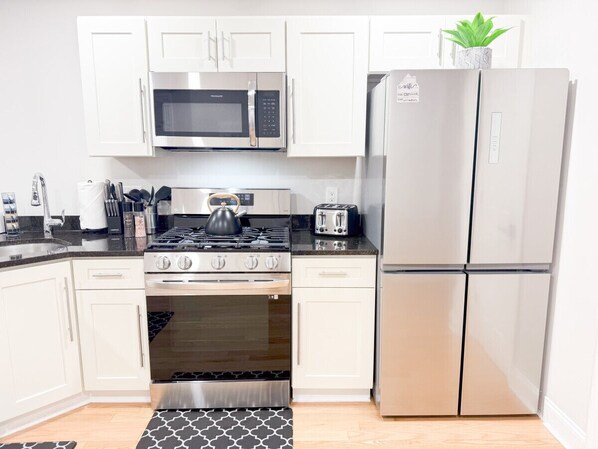 A kitchen with white cabinets, a stainless steel refrigerator, a microwave, a stove, and a toaster. - Modern, All New 3BR Near UMASS (Lowell)