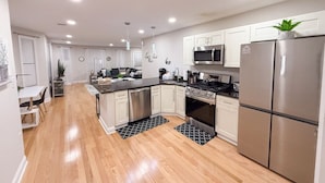 A modern kitchen with stainless steel appliances, wooden flooring, and white cabinetry. - Modern, All New 3BR Near UMASS (Lowell)