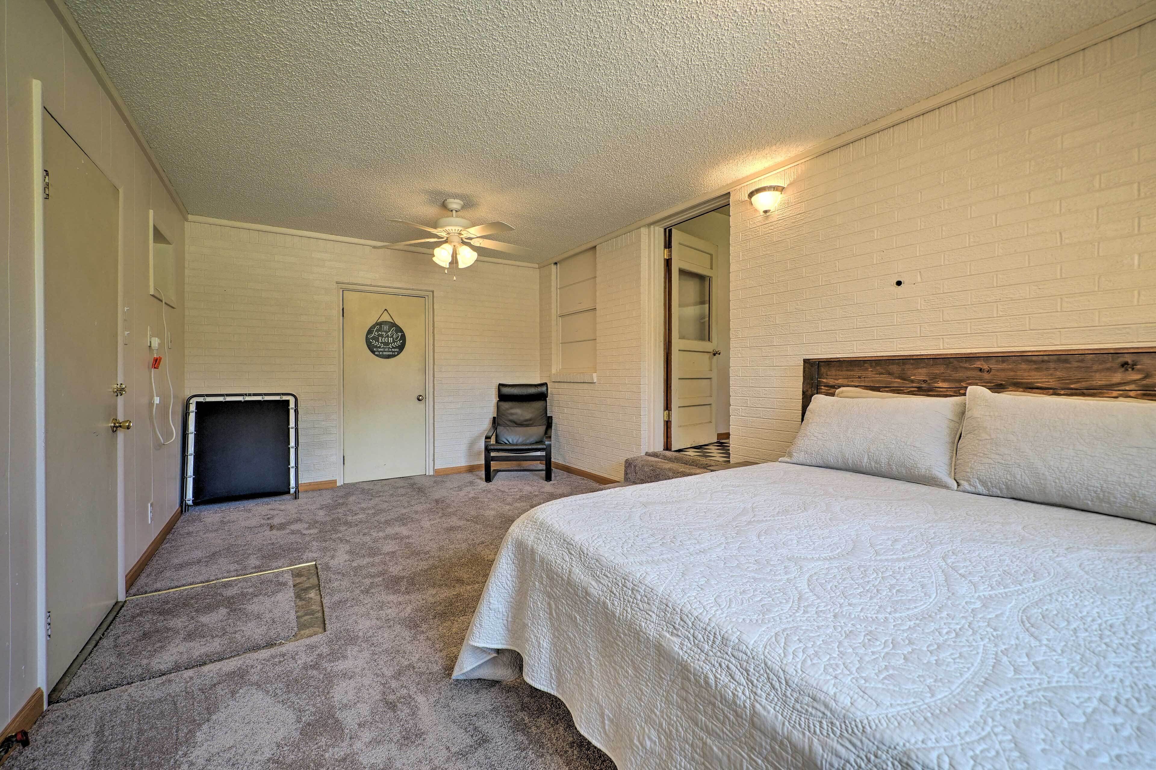 Ein Schlafzimmer mit einem großen Bett, einem Sessel, einem Deckenventilator und einer Tür zu einem anderen Raum.