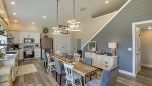 Une cuisine moderne avec des meubles blancs, une table à manger en bois et un escalier menant à une mezzanine.