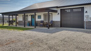 Un bâtiment doté d’un espace extérieur couvert aménagé en coin salon, d’un garage et d’une allée en gravier.