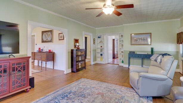 A spacious living room with hardwood flooring, a ceiling fan, a red cabinet, a beige armchair, and a large TV. - Charming Georgetown Home - Walk to Downtown! (Georgetown)