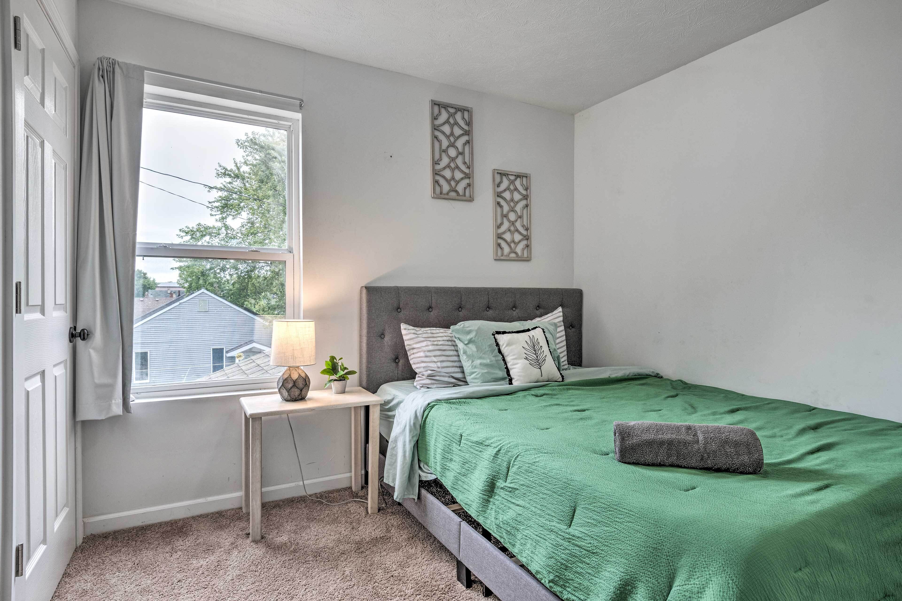 A bedroom with a bed, a nightstand, a lamp, and a window.