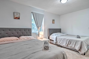 Quarto de hotel com duas camas, uma janela com cortinas, mesa de cabeceira com abajur e obras de arte nas paredes.
