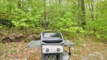 Un barbecue portable installé dans une zone boisée, avec un sentier en pierre et un feuillage verdoyant en arrière-plan.