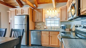 A kitchen with wooden cabinets, a stainless steel refrigerator, a dishwasher, granite countertops, and a window with curtains.