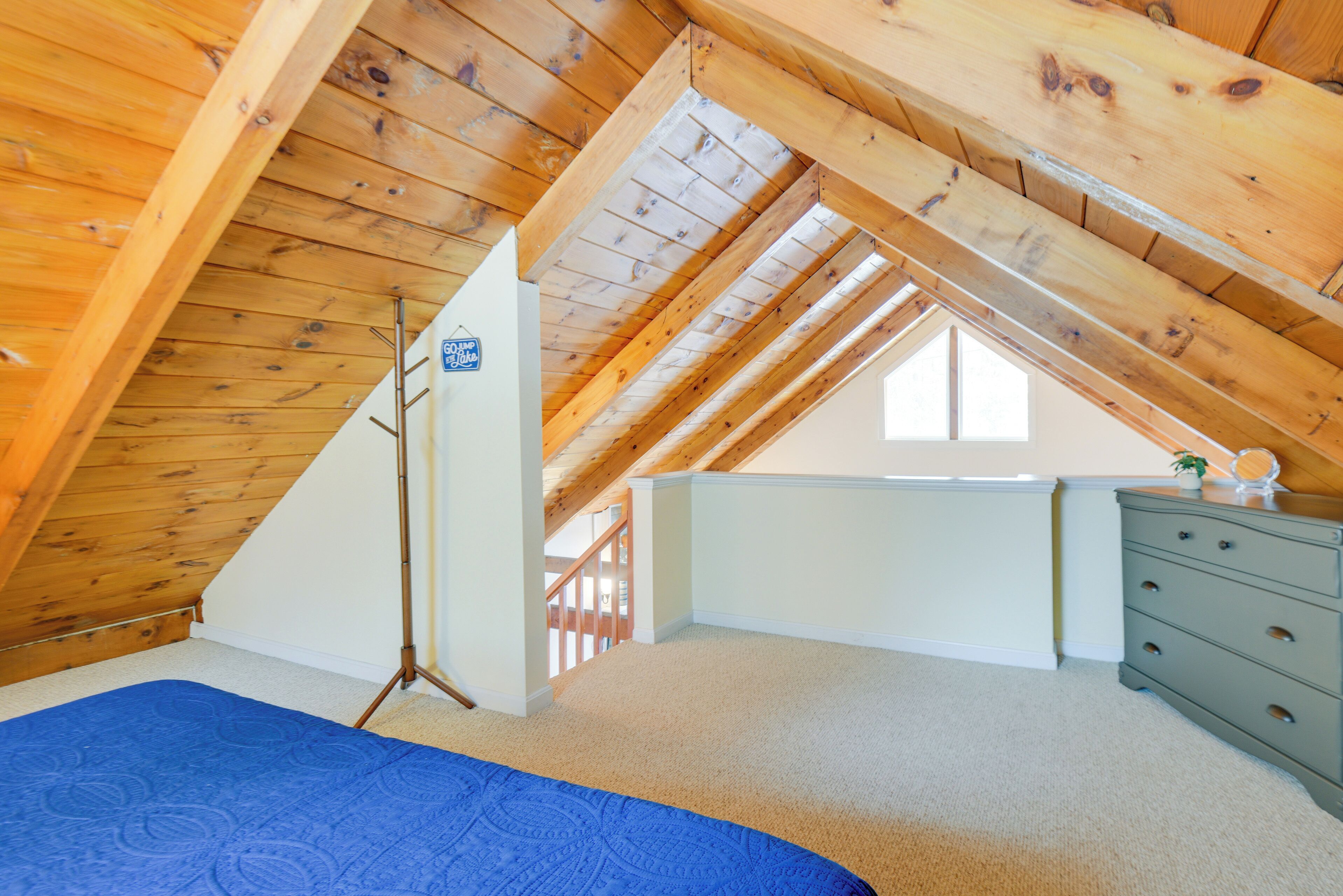 A bedroom with a sloped ceiling, a bed, a dresser, and a window.