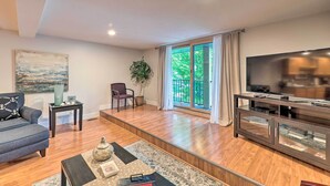 A modern living room with a sofa, a TV, and a glass cabinet. - Cute Grand Haven Apartment: Walk Downtown Streets! (Grand Haven)