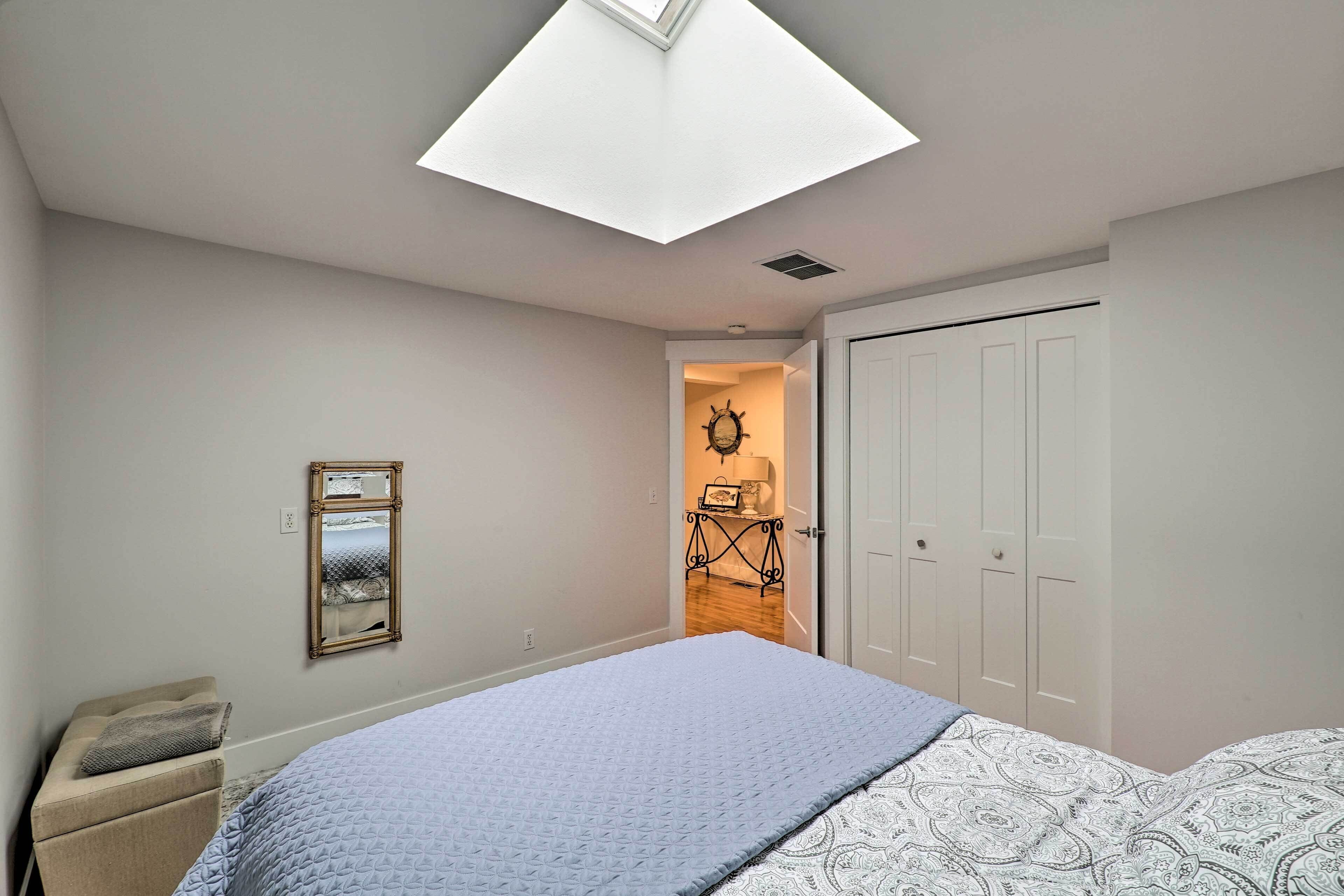 A bedroom with a skylight, a bed with patterned bedding, a bedside table, a chair, and a wardrobe.