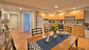 A modern kitchen with wooden cabinets, a dining table with chairs, and a vase of flowers. - Cute Grand Haven Apartment: Walk Downtown Streets! (Grand Haven)