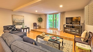 A living room with a sofa set, a coffee table, a television, and a large window with curtains. - Cute Grand Haven Apartment: Walk Downtown Streets! (Grand Haven)