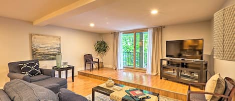 A living room with a sofa set, a coffee table, a television, and a large window with curtains.