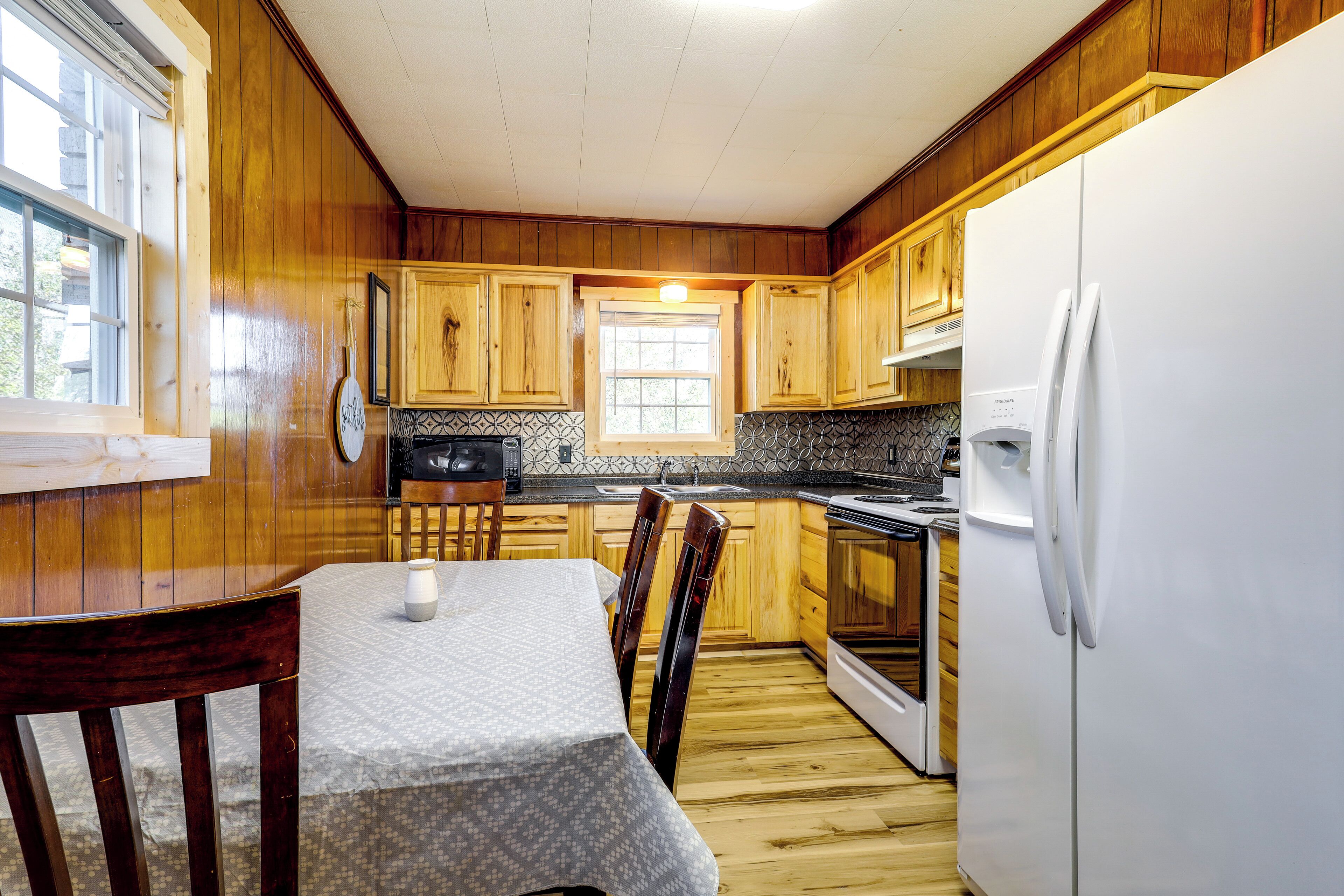 A kitchen with wooden cabinets, a white refrigerator, a dining table with chairs, and a window.