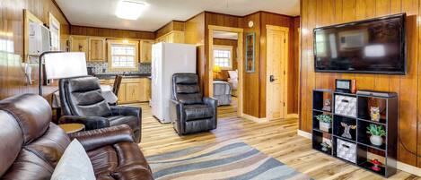 A spacious living room with a brown leather couch, a black leather chair, and a television on the wall.